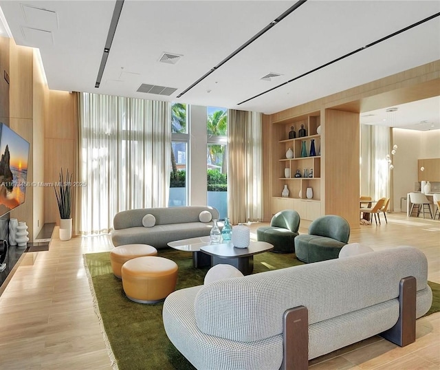 living room with built in shelves, a wall of windows, and light hardwood / wood-style floors