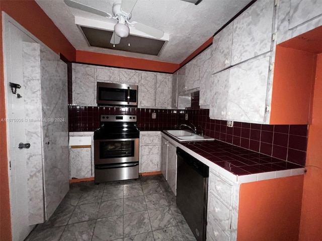 kitchen with ceiling fan, sink, tile counters, stainless steel appliances, and a textured ceiling