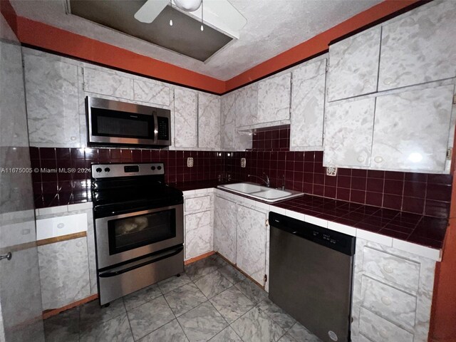 kitchen featuring ceiling fan, sink, stainless steel appliances, tile countertops, and white cabinetry