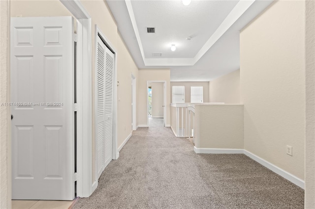 hallway with a raised ceiling and light colored carpet