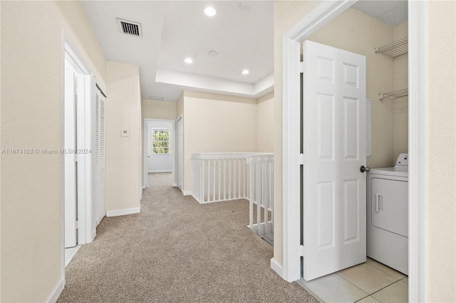 hall with washer / clothes dryer, light colored carpet, and a raised ceiling