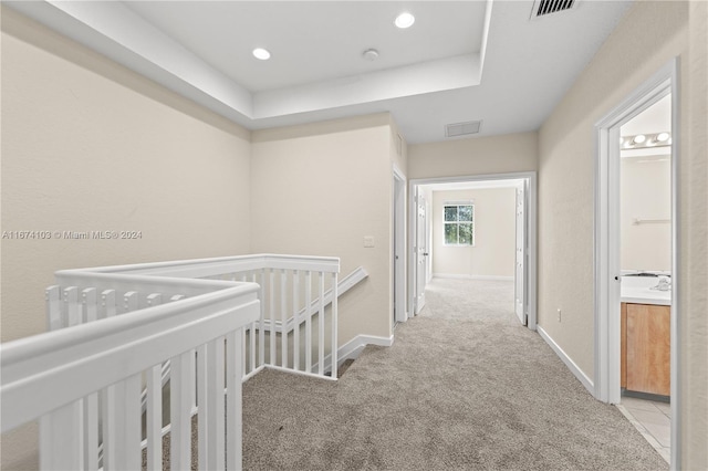 hall with a tray ceiling and light colored carpet