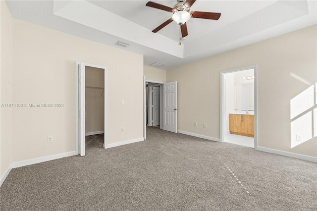 unfurnished bedroom featuring a walk in closet, ensuite bathroom, ceiling fan, light colored carpet, and a raised ceiling