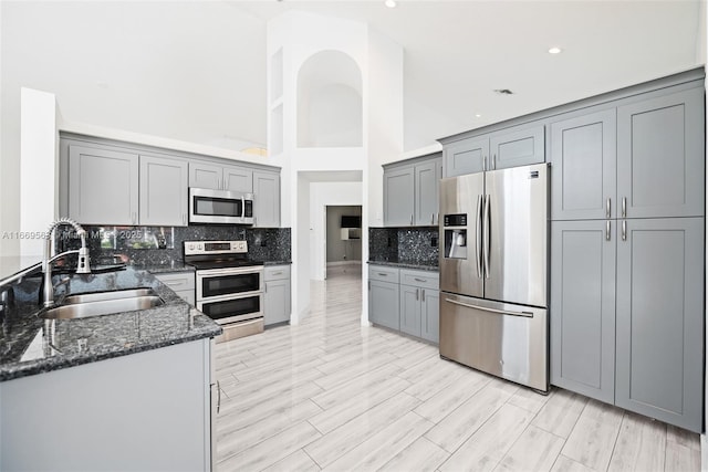 kitchen featuring gray cabinetry, sink, dark stone countertops, a towering ceiling, and stainless steel appliances