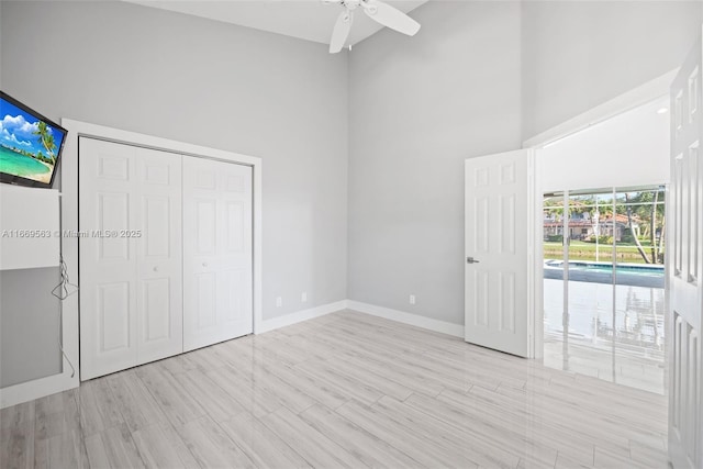 unfurnished bedroom featuring ceiling fan, light hardwood / wood-style floors, a towering ceiling, and a closet