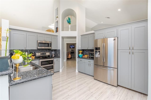 kitchen featuring high vaulted ceiling, dark stone counters, decorative backsplash, gray cabinets, and stainless steel appliances