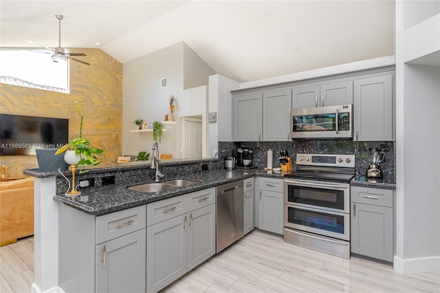 kitchen featuring sink, stainless steel appliances, kitchen peninsula, dark stone counters, and lofted ceiling