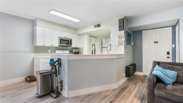 kitchen with light wood finished floors, tasteful backsplash, stainless steel microwave, visible vents, and white cabinets