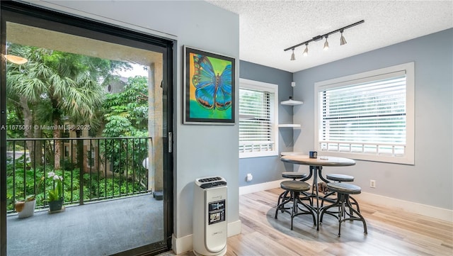 dining space featuring a textured ceiling, wood finished floors, baseboards, heating unit, and rail lighting