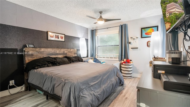 bedroom with ceiling fan, light hardwood / wood-style floors, and a textured ceiling