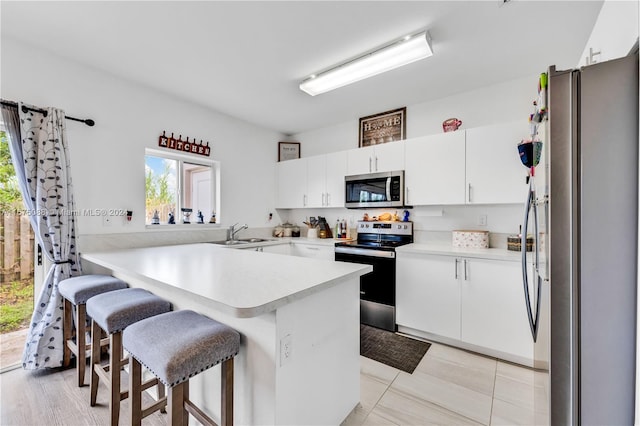 kitchen with kitchen peninsula, white cabinets, a breakfast bar, sink, and stainless steel appliances