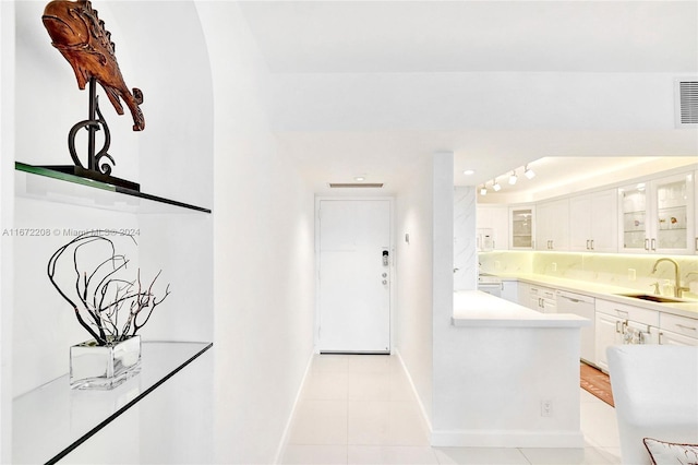 interior space featuring white dishwasher, white cabinetry, sink, and light tile patterned floors