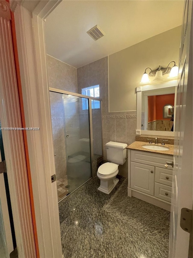 bathroom featuring toilet, tile walls, vanity, and walk in shower