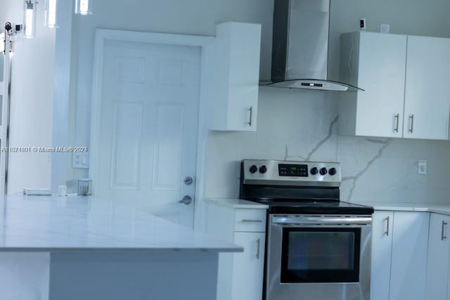 kitchen featuring wall chimney exhaust hood, light stone countertops, stainless steel range with electric stovetop, and white cabinetry