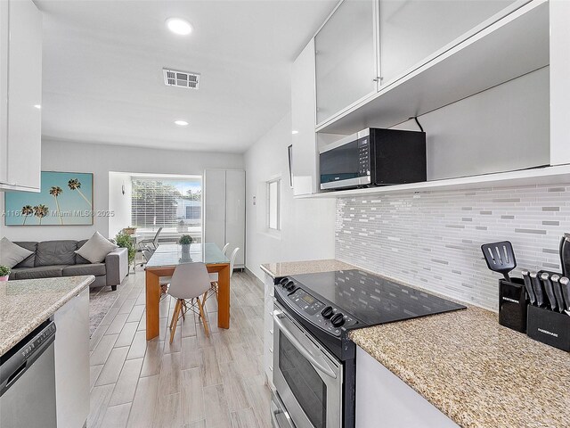 kitchen with white cabinetry, backsplash, stainless steel appliances, and light wood-type flooring