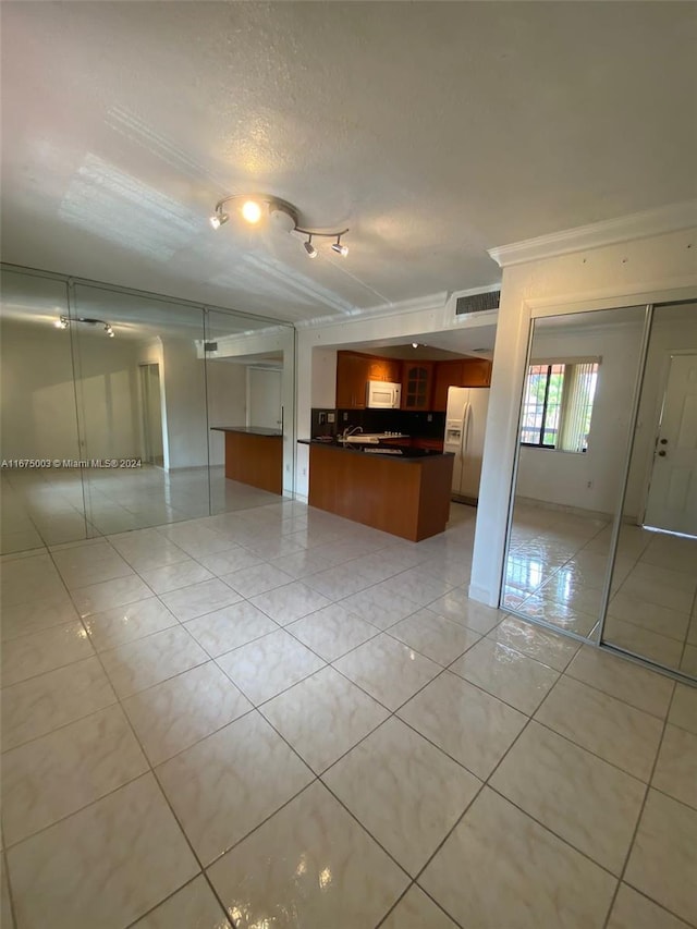 kitchen featuring white appliances, sink, kitchen peninsula, light tile patterned floors, and a textured ceiling