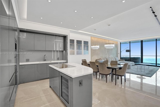 kitchen featuring a water view, gray cabinetry, beverage cooler, a center island, and black electric stovetop