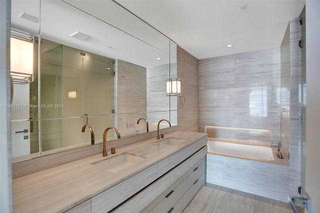 bathroom featuring a relaxing tiled tub, vanity, and tile walls