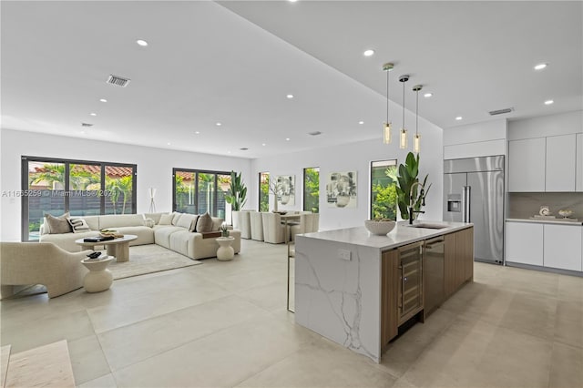 kitchen with light stone counters, hanging light fixtures, a center island with sink, white cabinetry, and appliances with stainless steel finishes