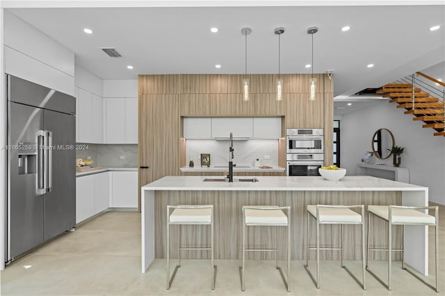 kitchen with an island with sink, tasteful backsplash, white cabinets, hanging light fixtures, and appliances with stainless steel finishes