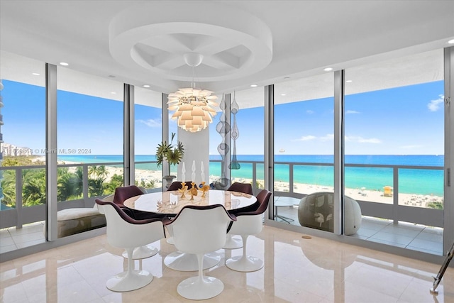 sunroom with a water view, a beach view, and an inviting chandelier