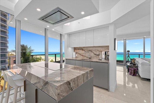 kitchen with a water view, sink, backsplash, white cabinets, and black stovetop