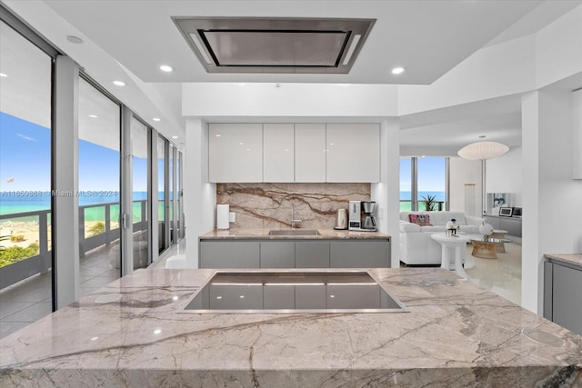 kitchen featuring black electric cooktop, light stone countertops, tasteful backsplash, sink, and white cabinetry