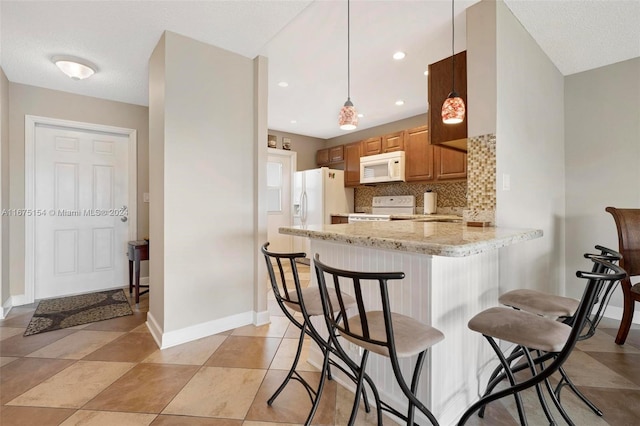 kitchen with hanging light fixtures, kitchen peninsula, backsplash, light stone counters, and white appliances