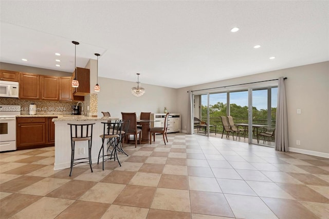 kitchen featuring backsplash, a kitchen bar, pendant lighting, light stone counters, and white appliances