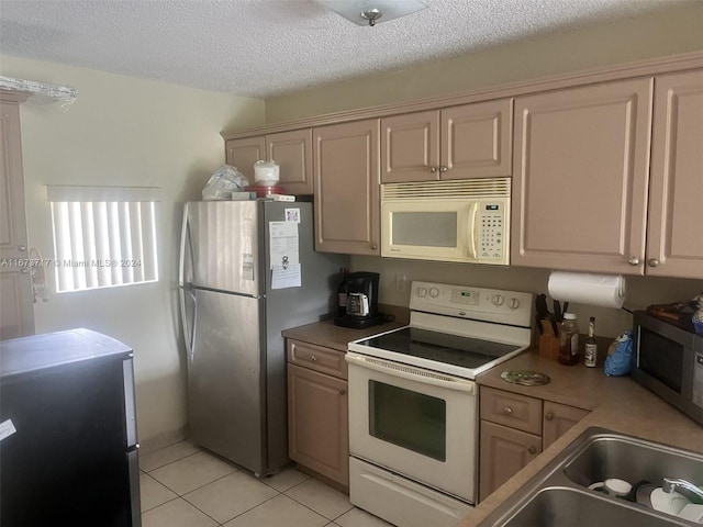 kitchen with light brown cabinets, light tile patterned flooring, sink, a textured ceiling, and appliances with stainless steel finishes