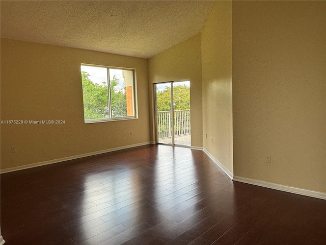 empty room with dark hardwood / wood-style floors, vaulted ceiling, and a textured ceiling