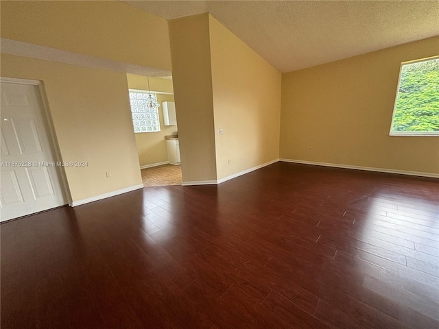 unfurnished room with dark wood-type flooring, lofted ceiling, and a textured ceiling