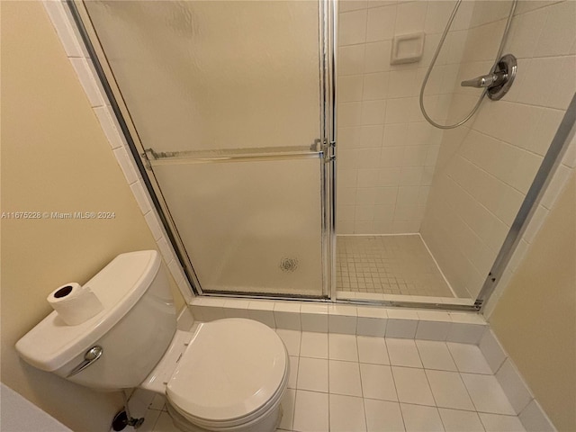 bathroom with tile patterned flooring, toilet, and a shower with shower door