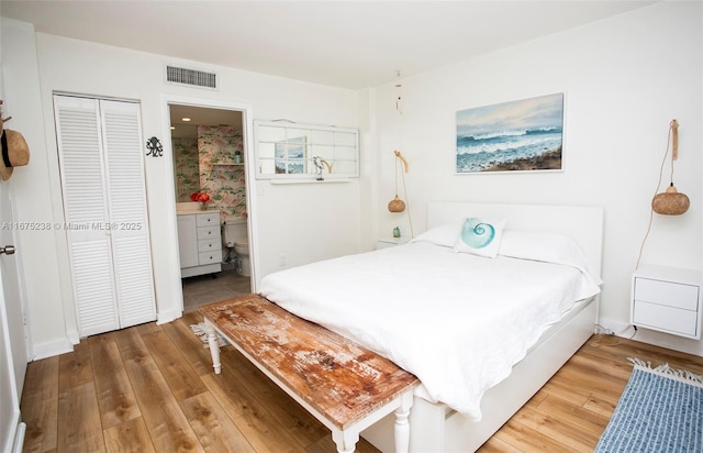 bedroom featuring ensuite bath, a closet, wood finished floors, and visible vents