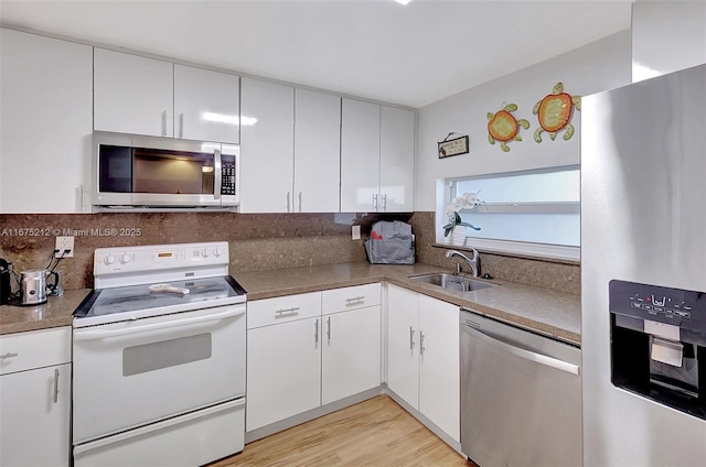 kitchen with appliances with stainless steel finishes, tasteful backsplash, sink, white cabinets, and light wood-type flooring