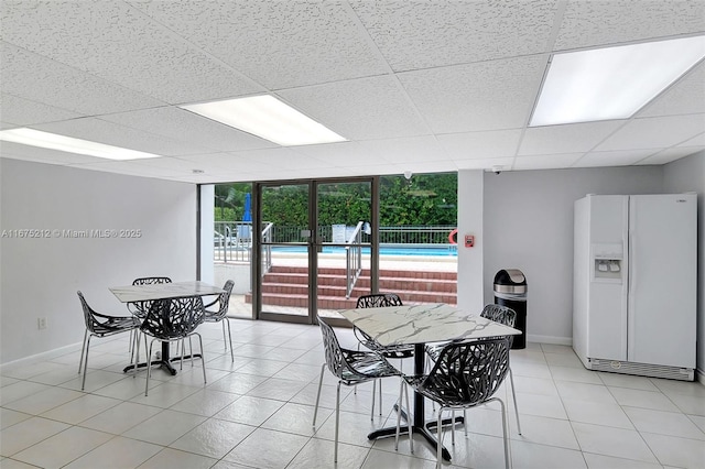 dining room featuring floor to ceiling windows, light tile patterned floors, and a drop ceiling