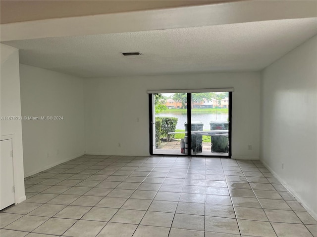 empty room with visible vents, a textured ceiling, a water view, and light tile patterned floors