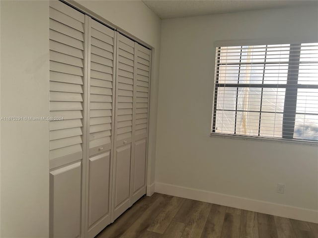unfurnished bedroom with dark wood-style flooring, baseboards, and a closet