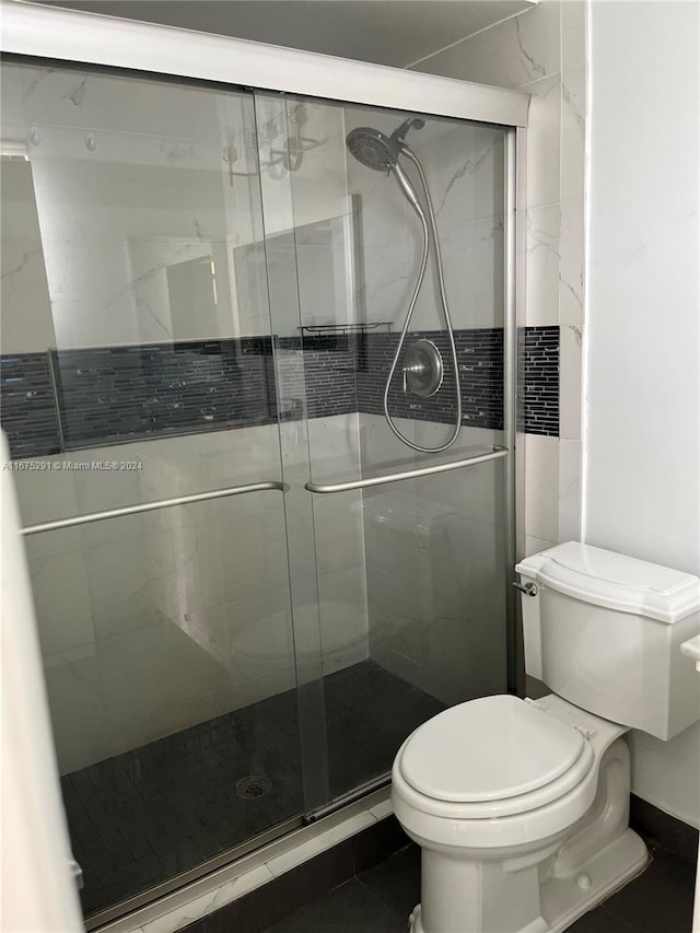 bathroom featuring tile patterned flooring, a shower with shower door, and toilet