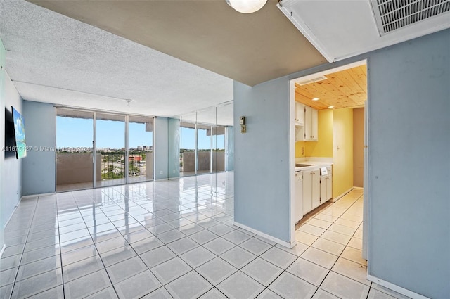 empty room with floor to ceiling windows, light tile patterned flooring, and a textured ceiling