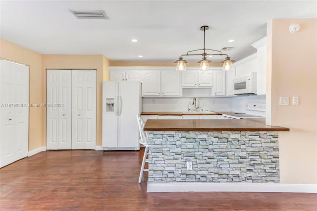 kitchen featuring white appliances, kitchen peninsula, white cabinetry, pendant lighting, and dark hardwood / wood-style floors