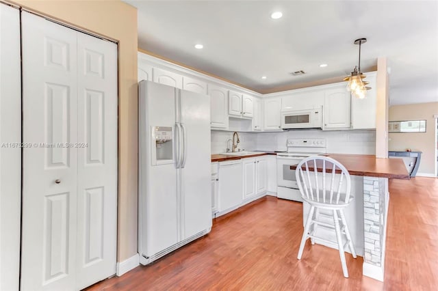 kitchen with white appliances, a kitchen bar, kitchen peninsula, pendant lighting, and white cabinets