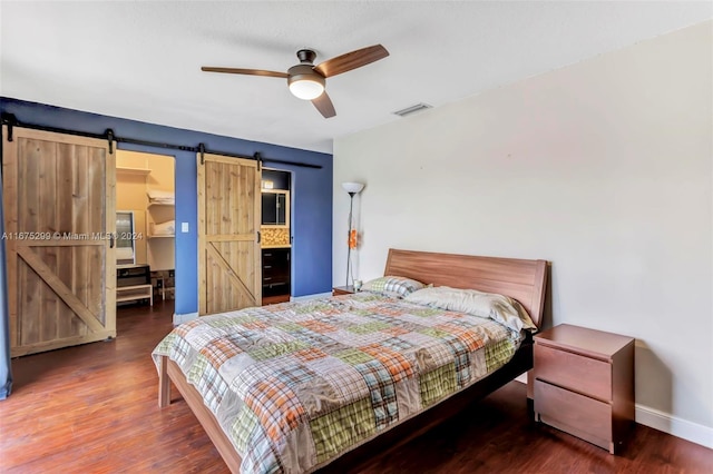 bedroom with ceiling fan, dark hardwood / wood-style floors, ensuite bathroom, and a barn door