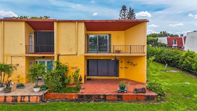 back of property with a balcony, a patio, and a lawn