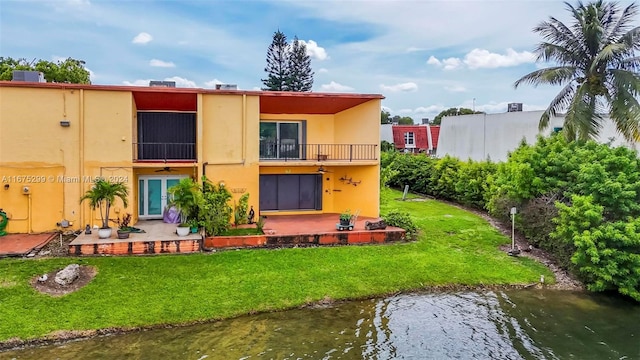 rear view of property featuring a patio, a lawn, a water view, and a balcony