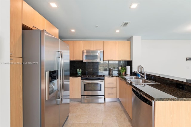 kitchen featuring stainless steel appliances, dark stone countertops, sink, light brown cabinetry, and backsplash