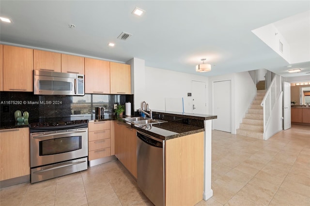 kitchen with dark stone countertops, sink, kitchen peninsula, appliances with stainless steel finishes, and backsplash