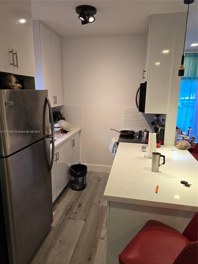 kitchen with white cabinets, electric range oven, decorative light fixtures, stainless steel refrigerator, and light wood-type flooring