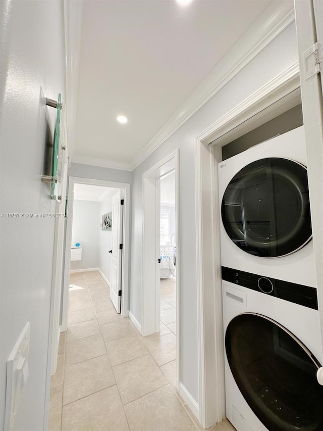 clothes washing area featuring ornamental molding, light tile patterned flooring, and stacked washer and clothes dryer