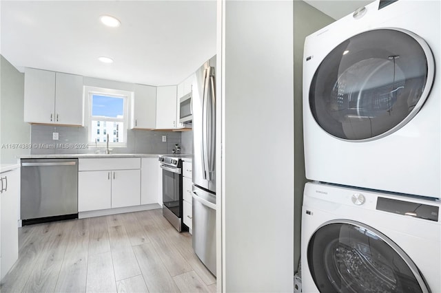 kitchen featuring white cabinetry, stacked washing maching and dryer, appliances with stainless steel finishes, and light wood-type flooring